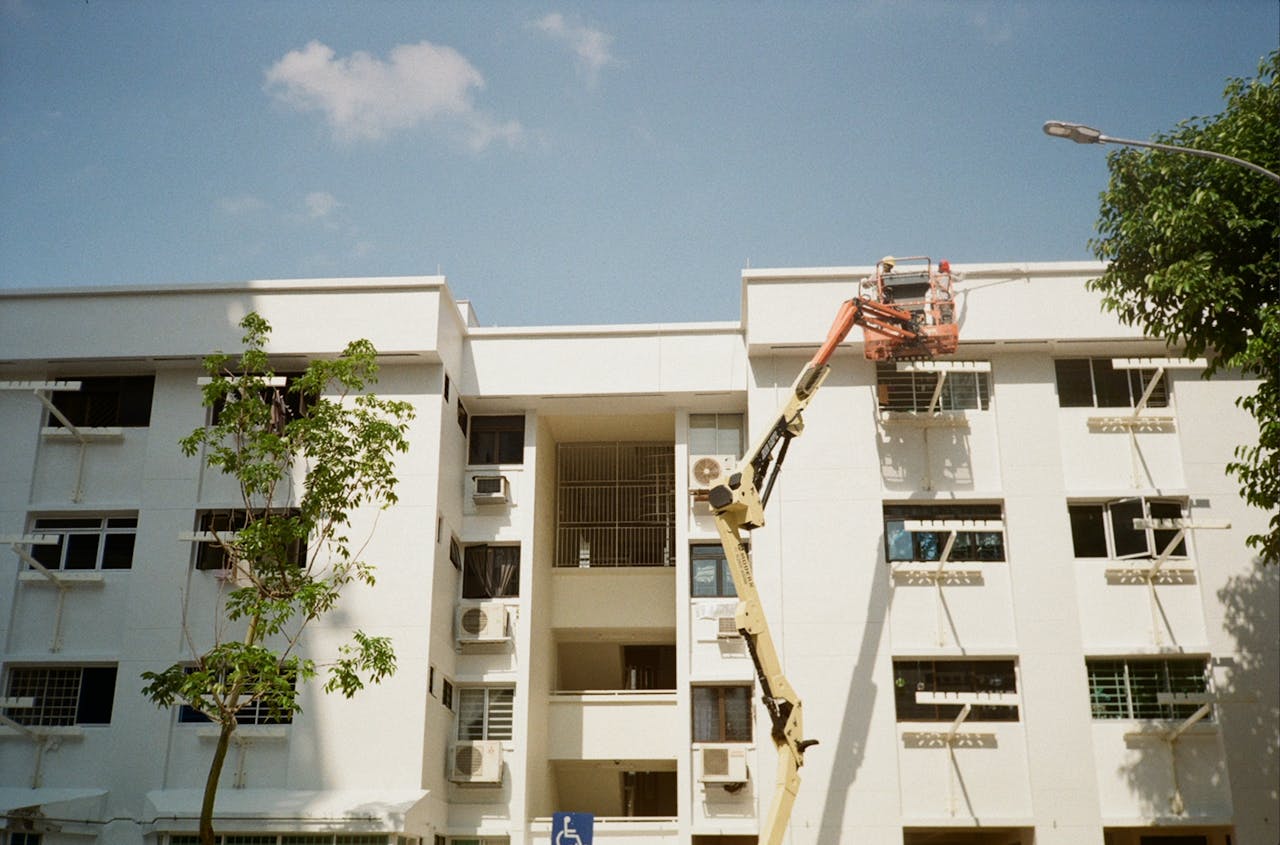 Services An exterior view of a residential building with maintenance work using a crane lift under clear blue skies.