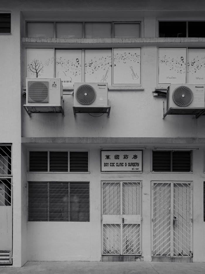 Services A black and white image of a clinic facade featuring air conditioning units and barred windows.